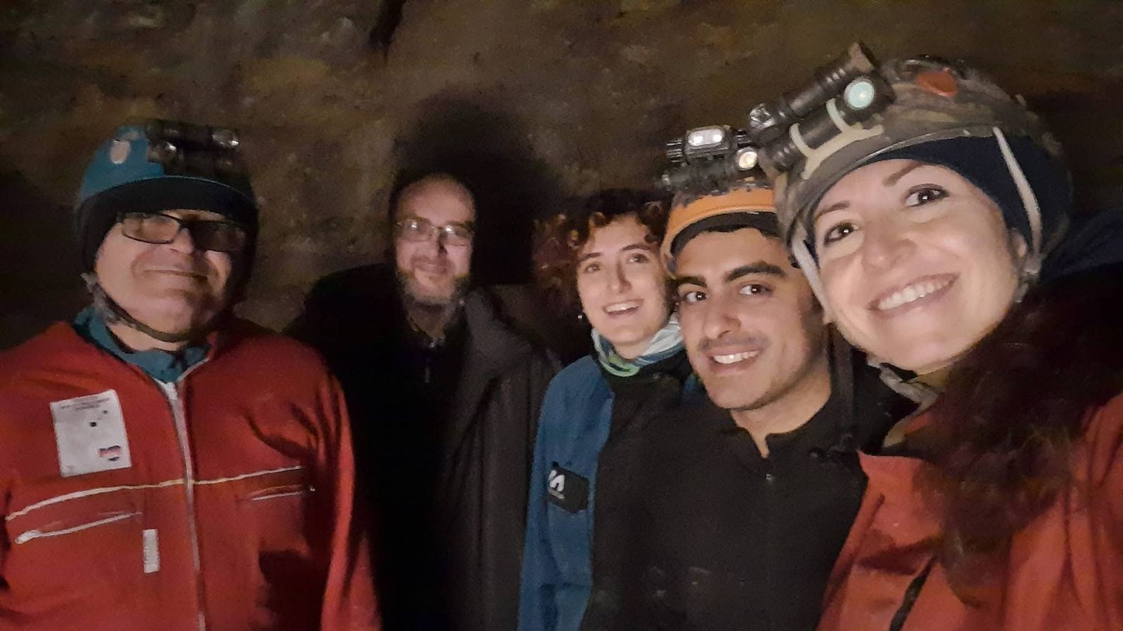 Cinque soci sorridenti con caschi e frontali in una galleria sotterranea